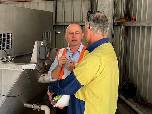 Qtech discussing wastewater treatment process improvements beside treatment equipment at a customer site.